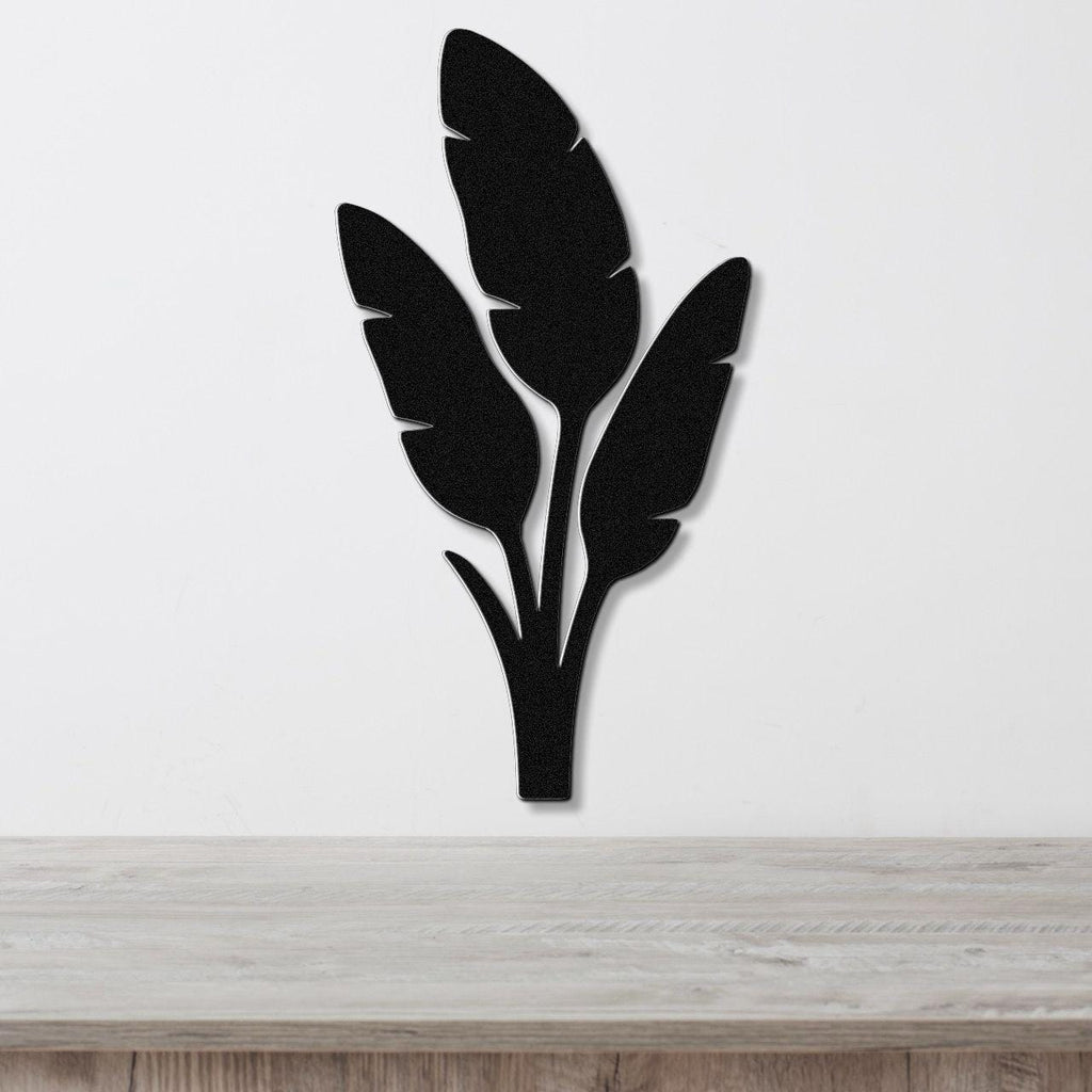 Black metal wall art in a tropical leaf silhouette design, mounted on a white wall above a light wood surface.