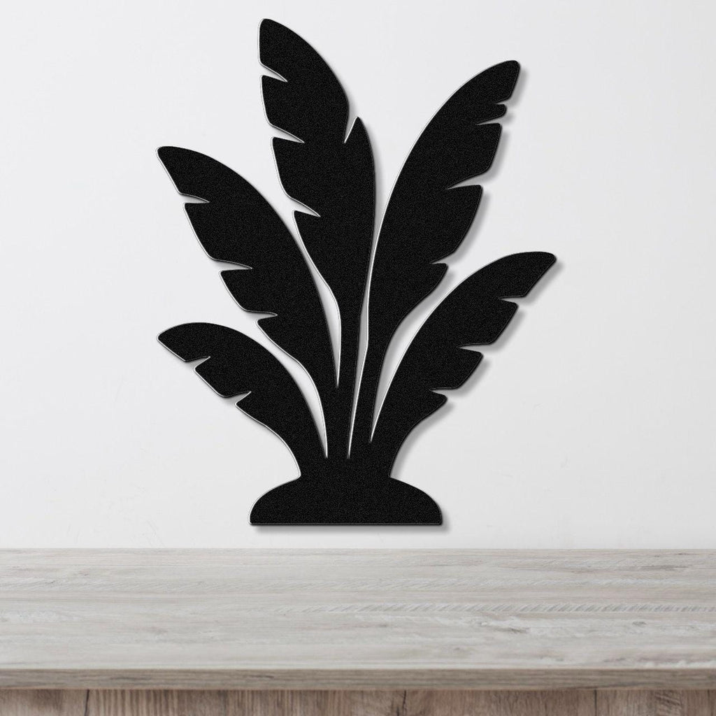 Black metal wall art in a tropical leaf silhouette design, mounted on a white wall above a light wood surface.