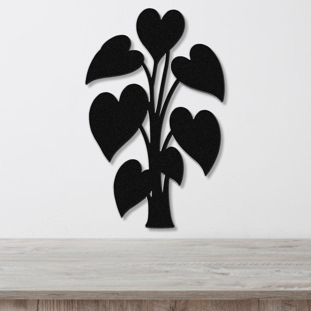 Black metal wall art in the shape of a heart-leaf plant, mounted on a white wall above a light wood surface.