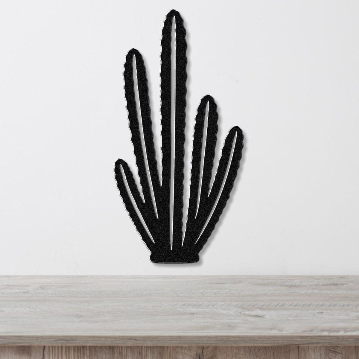 Black metal wall art cutout of an organ pipe cactus with multiple vertical arms, mounted on a white wall above a light wood surface.