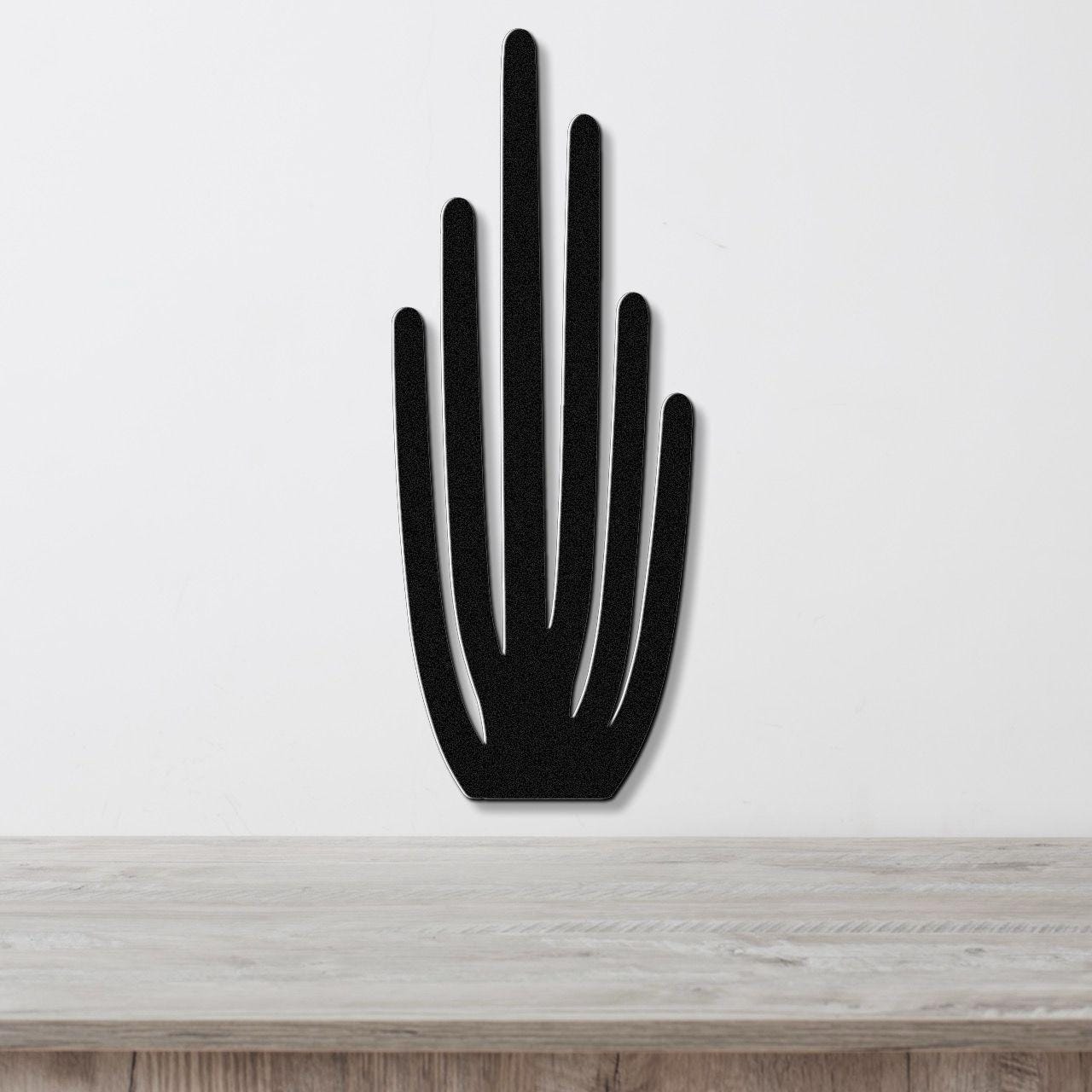 Black metal wall art cutout of an organ pipe cactus with vertical spines, mounted on a white wall above a light wood surface.
