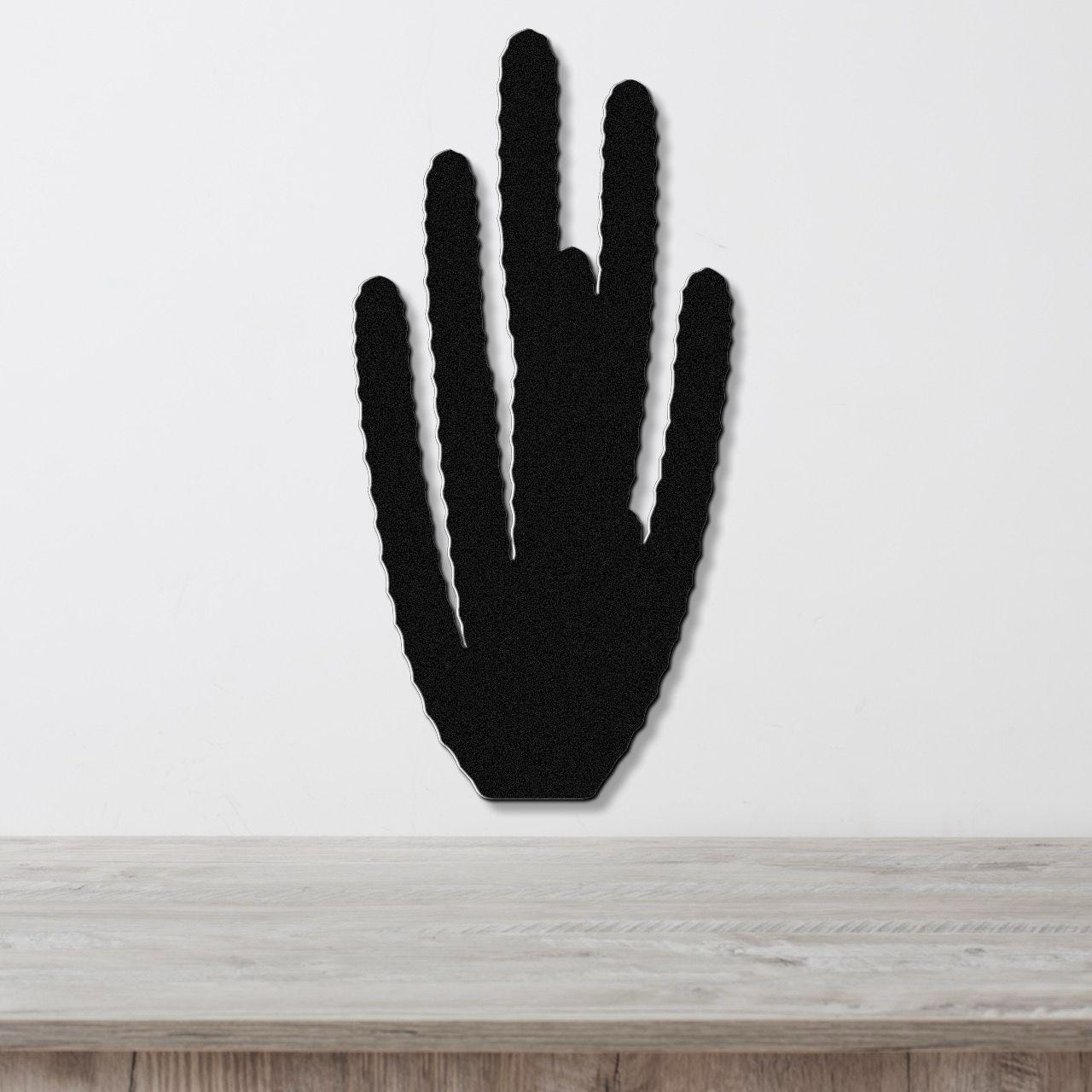 Black metal wall art cutout of an organ pipe cactus with vertical spines, mounted on a white wall above a light wood surface.