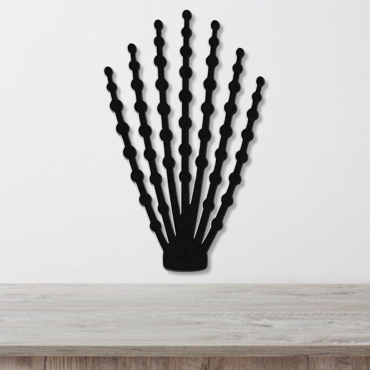 Black metal ocotillo wall art with beaded branch cutouts, mounted on a white wall above a light wood counter.