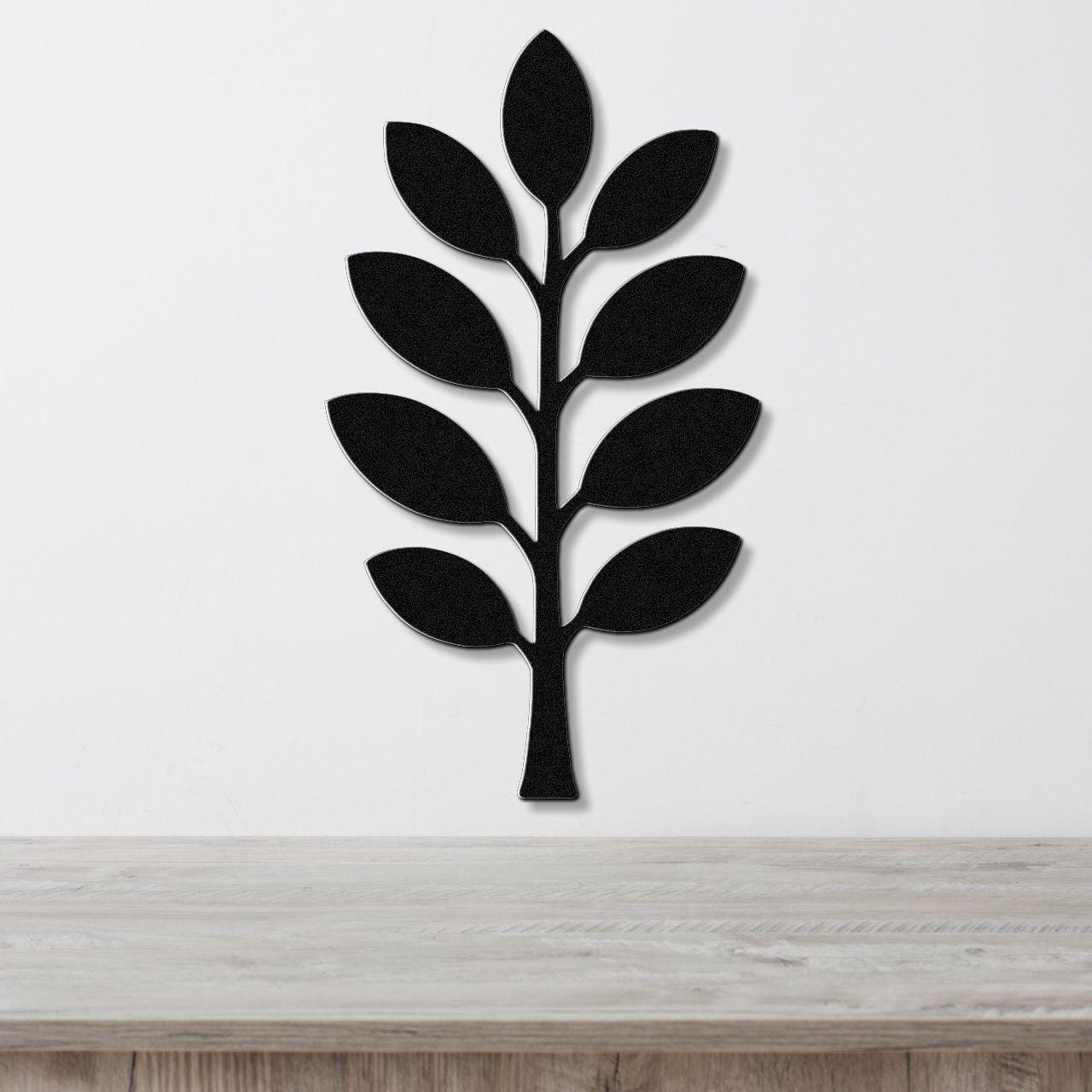 Black metal wall art in the shape of an olive branch with leaf cutouts, mounted on a white wall above a light wood surface.