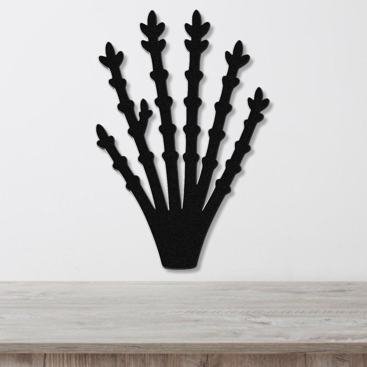 Black metal ocotillo wall art with branching cutouts, mounted on a white wall above a light wood surface.