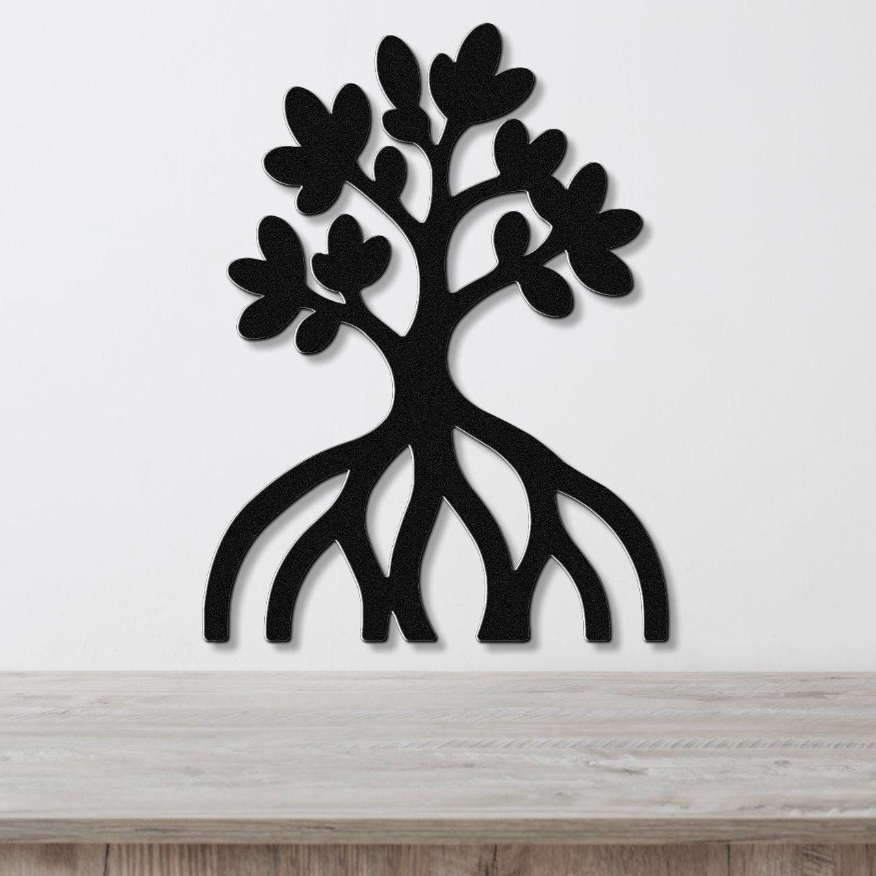 Black metal wall art cutout of a mangrove tree with visible roots and leafy branches, mounted on a white wall above a wooden surface.