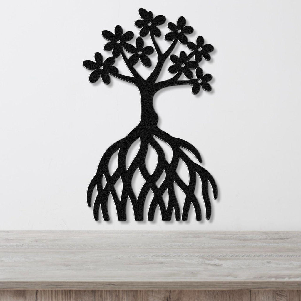 Black metal wall art cutout of a tree with flower blossoms and exposed roots, mounted on a white wall above a wooden surface.