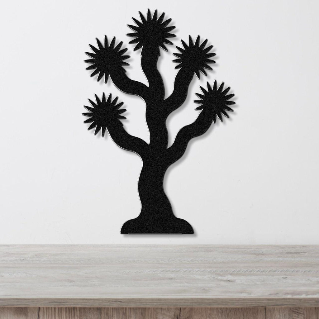 Black metal wall art in the silhouette of a Joshua tree with starburst-shaped branches, mounted on a white wall above a light wood surface.