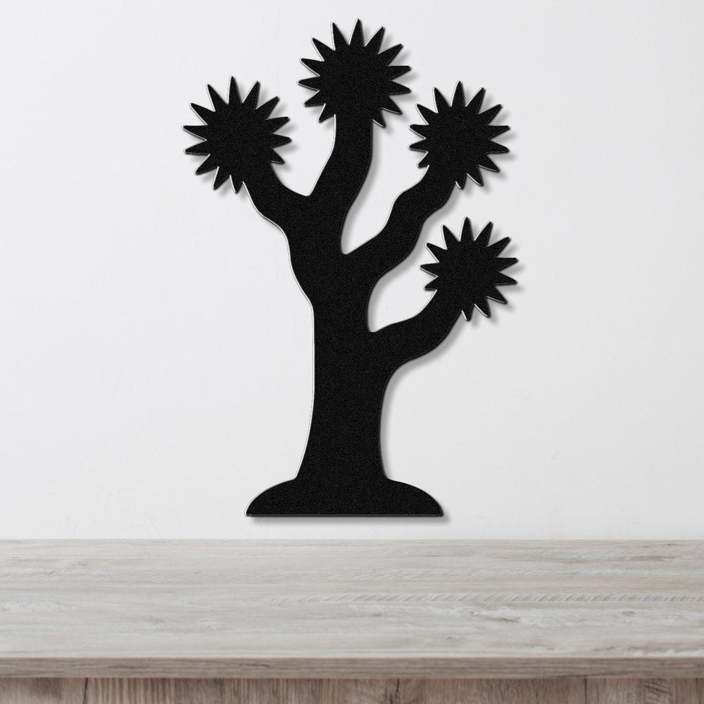 Black metal Joshua tree wall art with starburst-shaped branches, mounted on a white wall above a light wood surface.