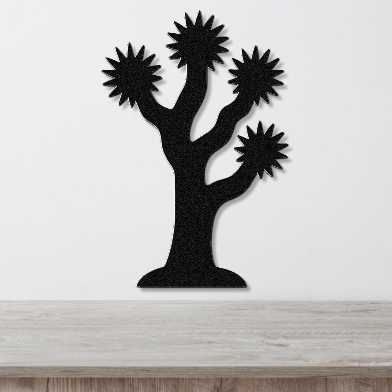 Black metal Joshua tree wall art with starburst-shaped branches, mounted on a white wall above a light wood surface.