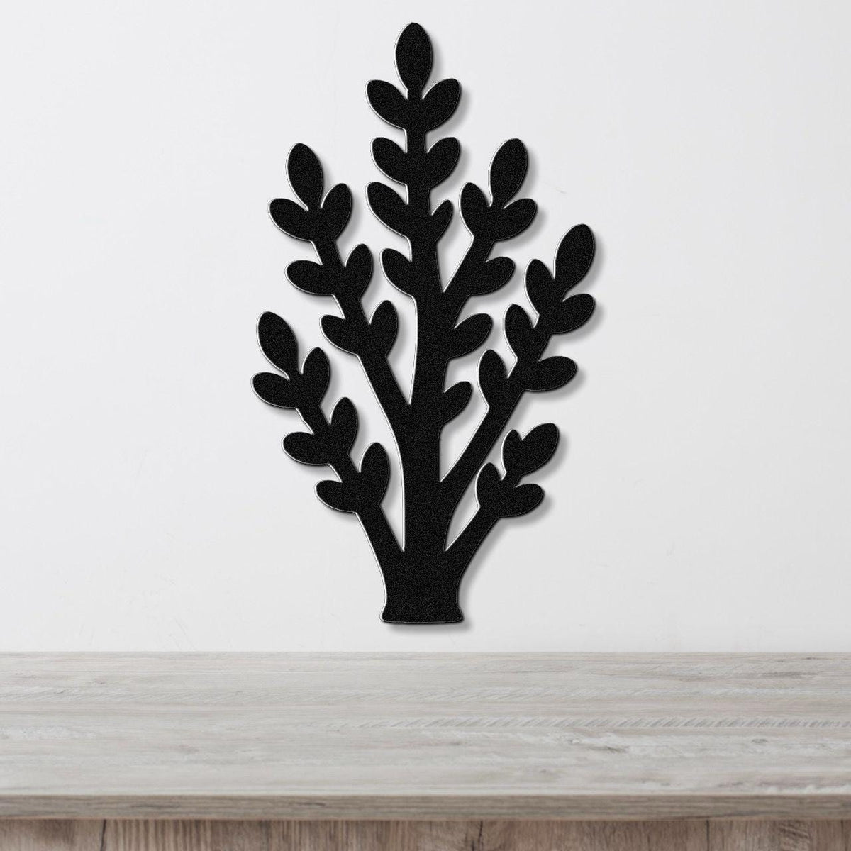 Black metal wall art in a jade plant silhouette with layered leaf cutouts, mounted on a white wall above a light wood surface.