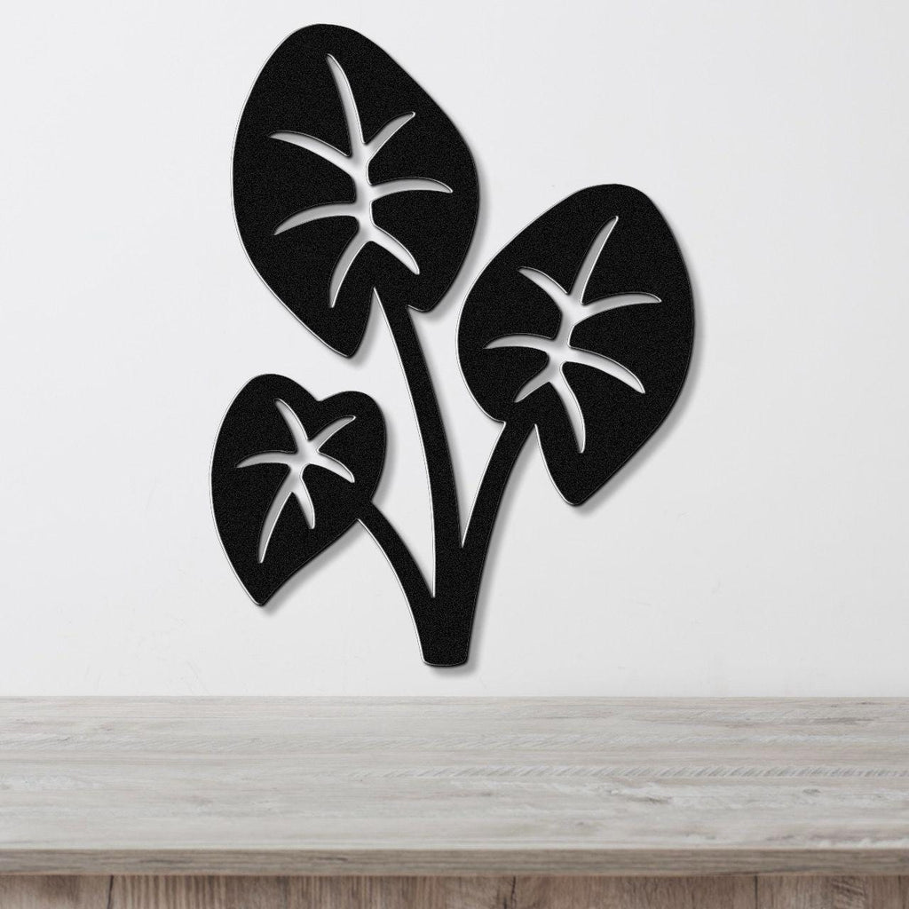 Black metal wall art featuring three elephant ear leaves with star-shaped cutouts, mounted on a white wall above a light wood surface.