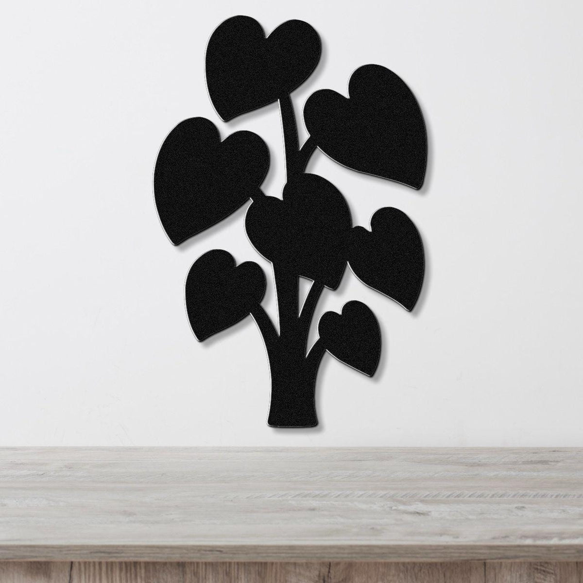 Black metal wall art shaped like a plant with heart-shaped leaves, mounted on a white wall above a wooden surface.