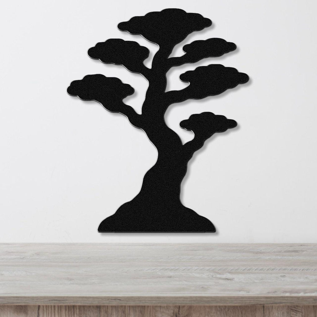 Black metal wall art in the silhouette of a bonsai tree with layered cloud-like branches, mounted on a white wall above a wooden surface.