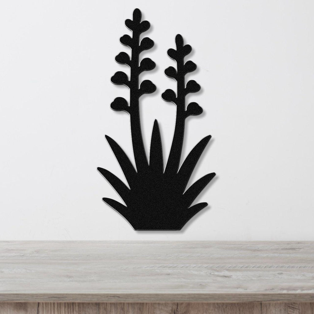 Black metal wall art cutout of a blooming agave plant with two tall flower stalks and spiky base, mounted on a white wall above a light wood surface.