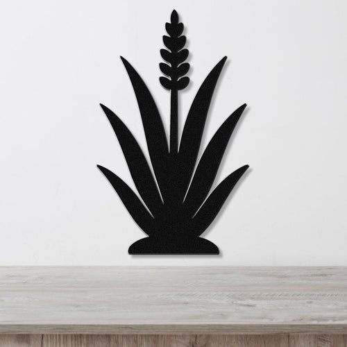 Black metal agave wall art with a central flower spike and leaf cutouts, mounted on a white wall above a light wood surface.