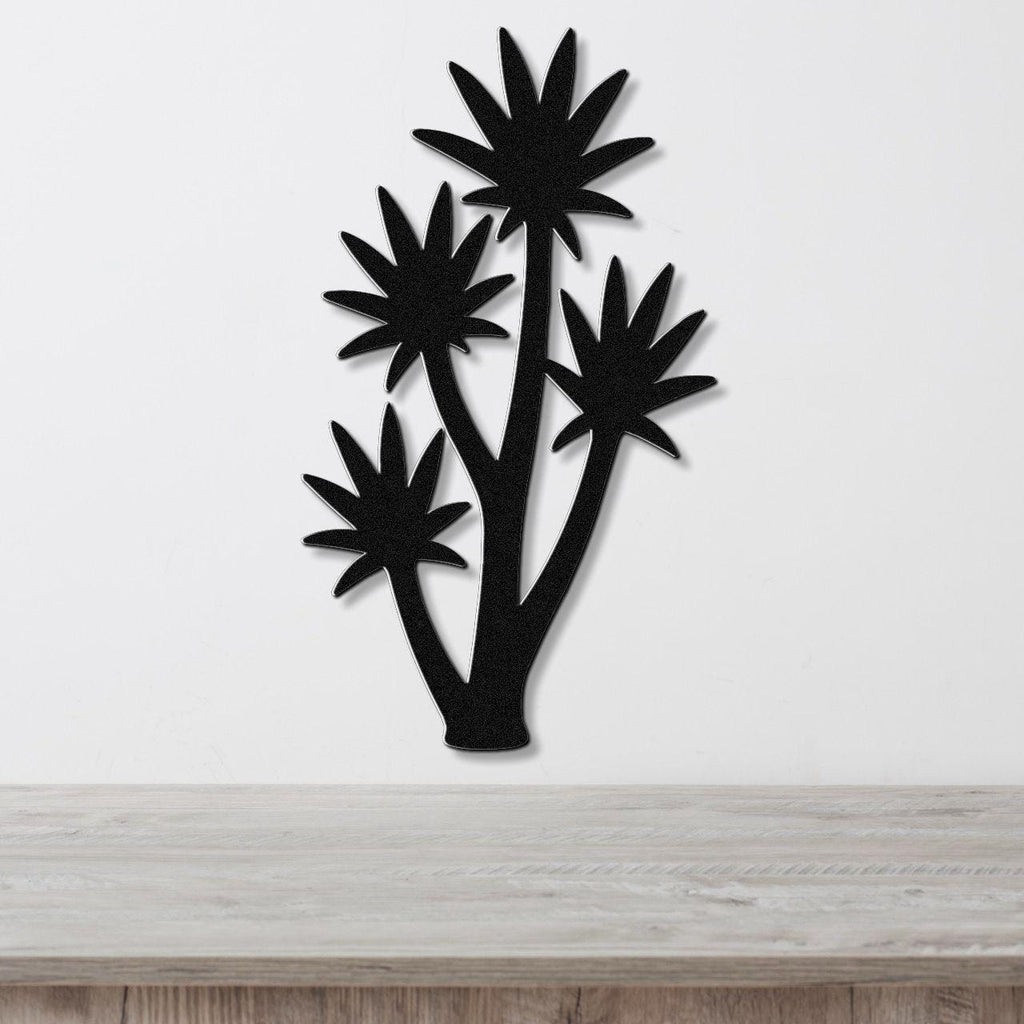 Black metal wall art cutout of a tall yucca plant with multiple star-shaped fronds, mounted on a white wall above a light wood surface.