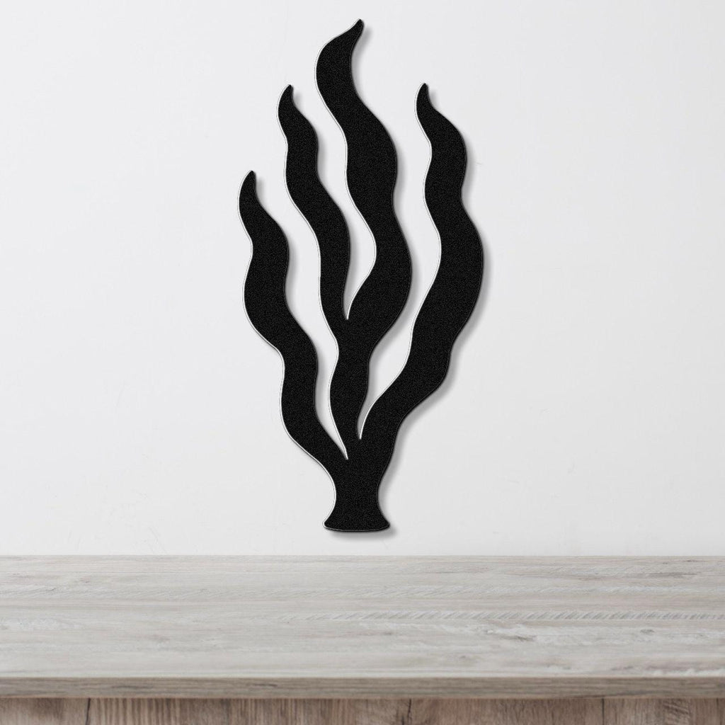 Black metal wall art in a kelp seaweed silhouette with layered fronds, mounted on a white wall above a light wood surface.