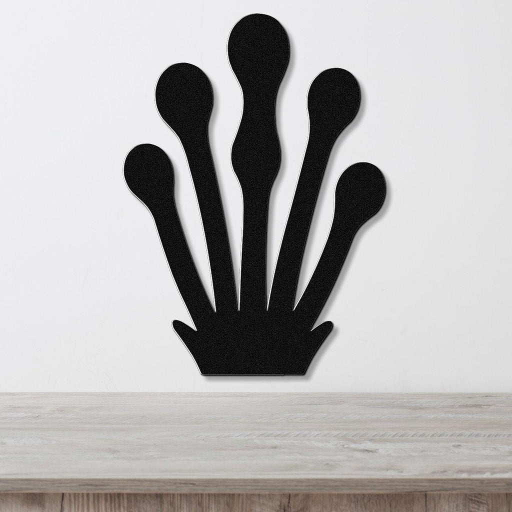 Black metal wall art in a kelp or seaweed silhouette design with five elongated fronds, mounted on a white wall above a light wood surface.
