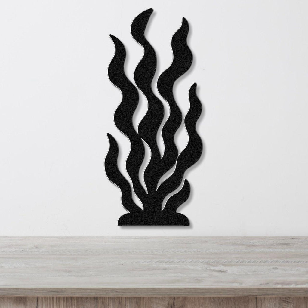 Black metal wall art in a seaweed or kelp silhouette design with layered, wavy cutouts, mounted on a white wall above a light wood surface.