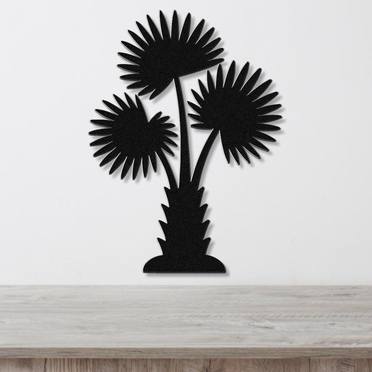 Black metal wall art cutout of a California fan palm tree with three fronds, mounted on a white wall above a light wood countertop.