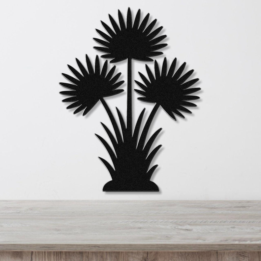 Black metal wall art cutout of a fan palm tree with three fronds and grassy base, mounted on a white wall above a wooden surface.