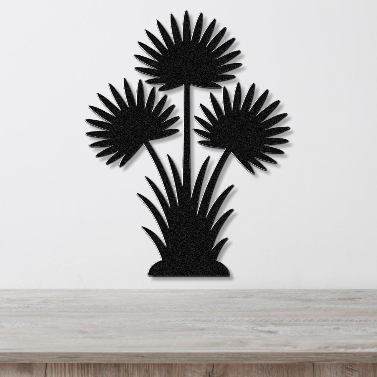 Black metal wall art cutout of a fan palm tree with three fronds and grassy base, mounted on a white wall above a wooden surface.