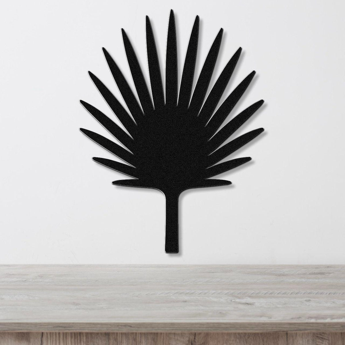 Black metal fan palm tree wall art with radiating leaf cutouts, mounted on a white wall above a light wood surface.