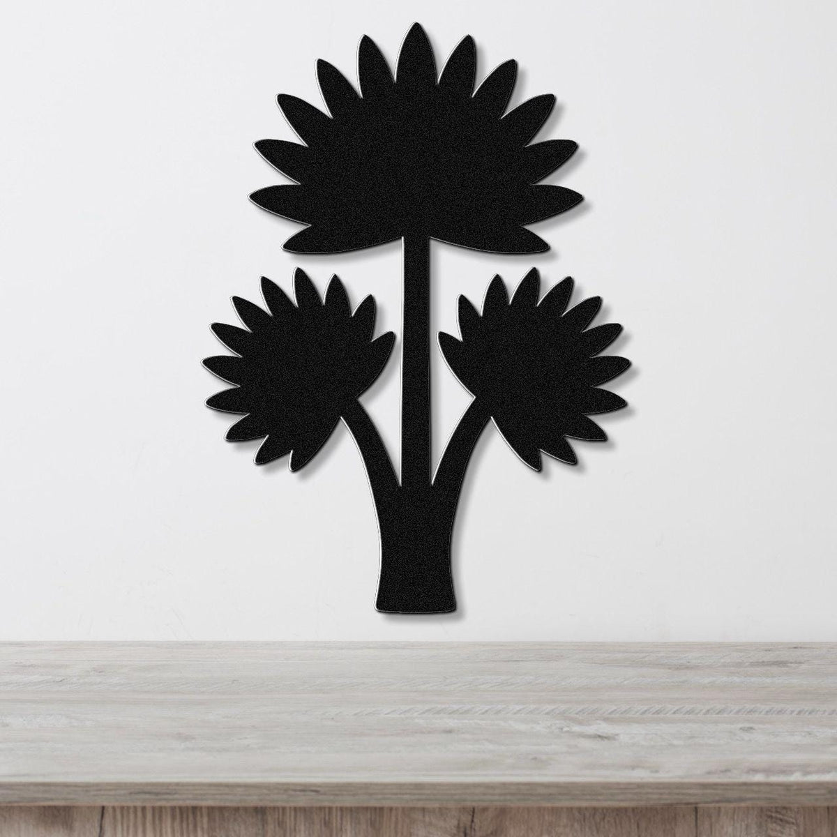 Black metal wall art in a fan palm tree silhouette with three leafy fronds, mounted on a white wall above a light wood surface.