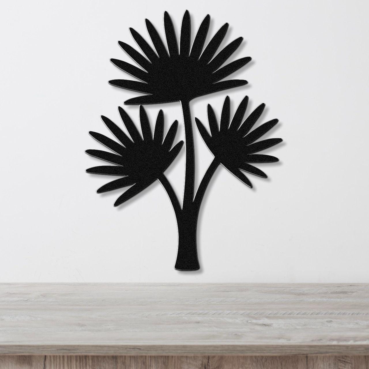 Black metal cutout wall art of a fan palm tree with three fronds, mounted on a white wall above a light wood countertop.