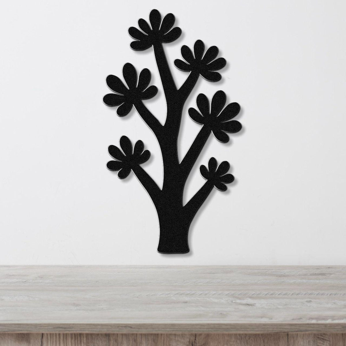 Black metal wall art in a tree silhouette with flower cutouts, mounted on a white wall above a light wood counter.