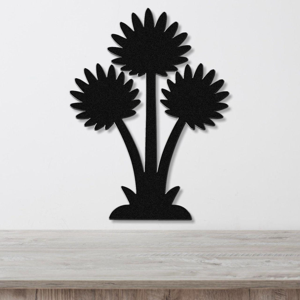 Black metal wall art cutout of three sunflower-like blooms with radiating petals, mounted on a white wall above a light wood surface.