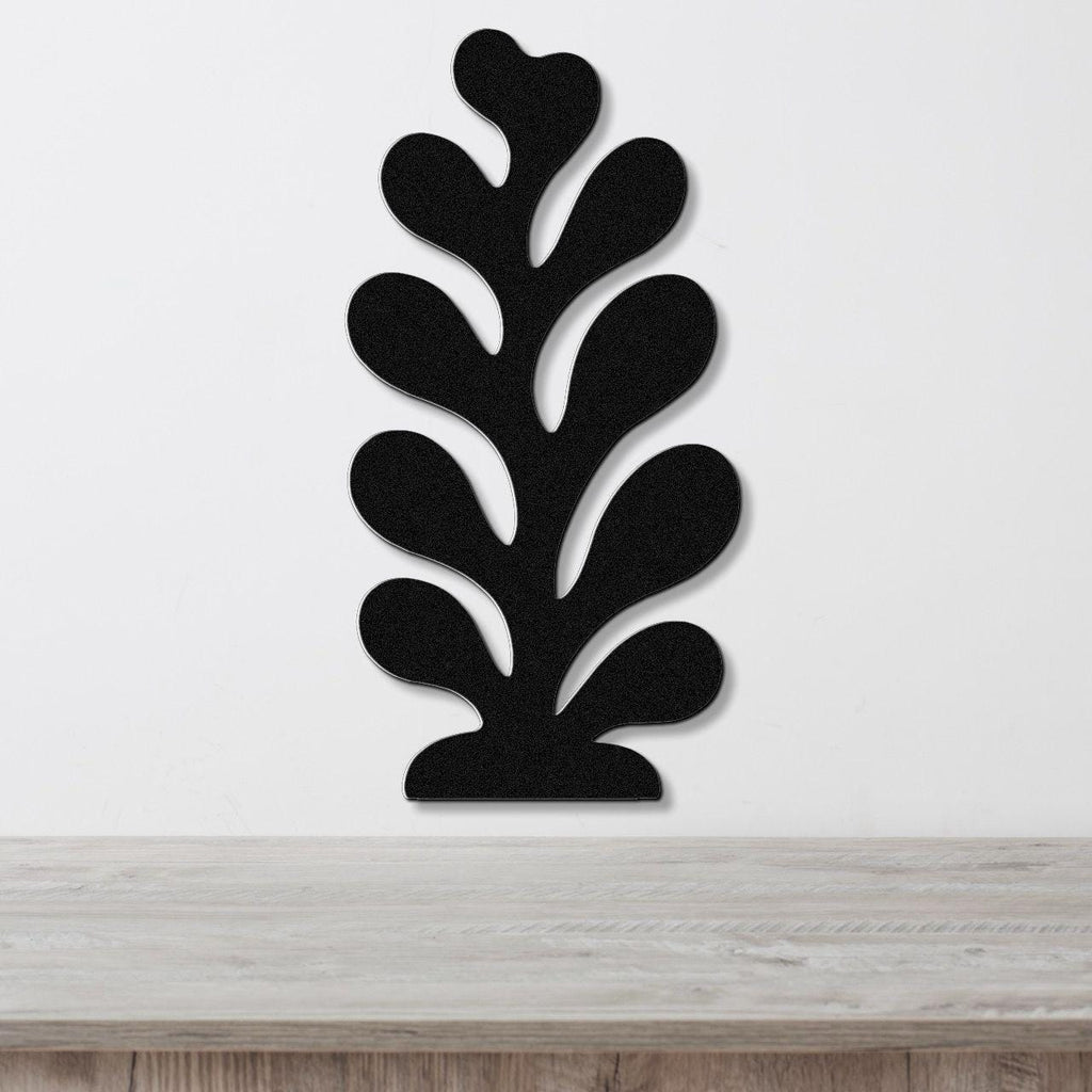 Black metal wall art in a coral or leaf-like silhouette with multiple cutout sections, mounted on a white wall above a light wood surface.