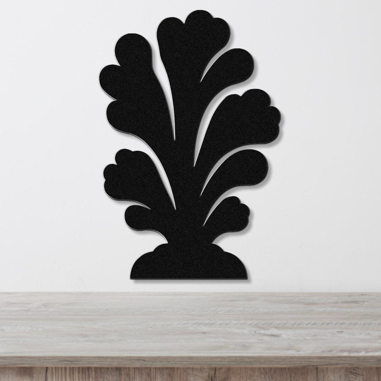 Black metal wall art in a coral silhouette design with layered, flowing cutouts, mounted on a white wall above a wooden surface.