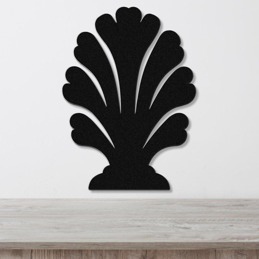 Black metal wall art in a coral or fan shape with layered, scalloped cutouts, mounted on a white wall above a light wood surface.
