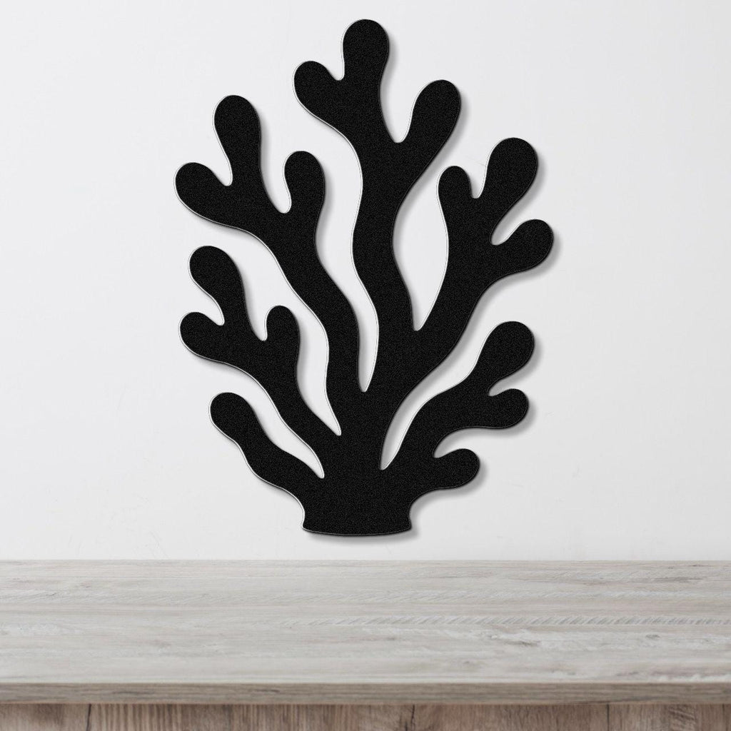 Black metal coral wall art with branching cutouts, mounted on a white wall above a light wood counter.