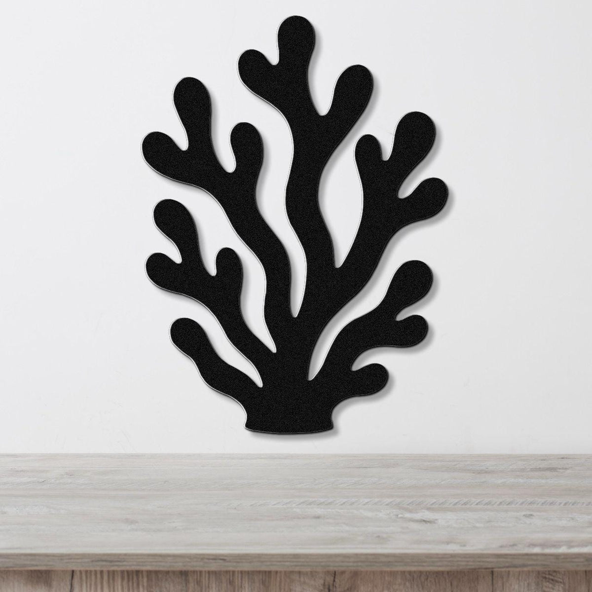 Black metal coral wall art with branching cutouts, mounted on a white wall above a light wood counter.