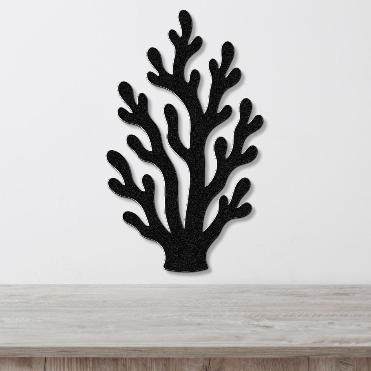 Black metal coral wall art with branching cutouts, mounted on a white wall above a light wood surface.