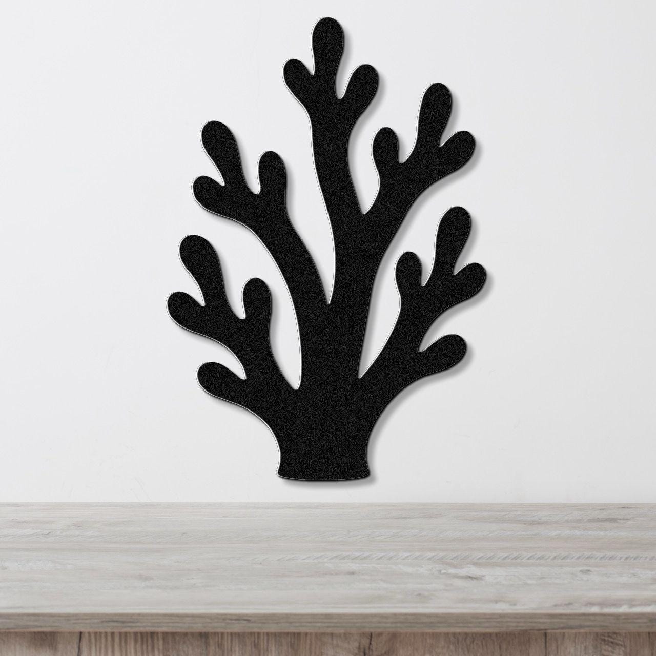Black metal wall art in a branching coral silhouette with multiple cutout arms, mounted on a white wall above a light wood surface.