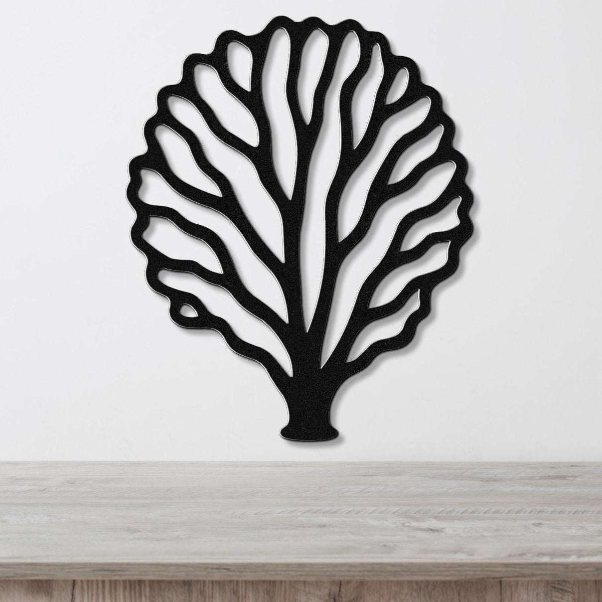 Black metal fan coral wall art with intricate cutout branches, mounted on a white wall above a light wood counter.