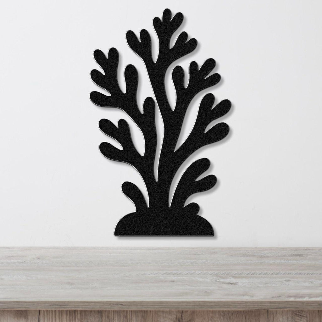 Black metal wall art in a coral silhouette design with branching cutouts, mounted on a white wall above a light wood surface.
