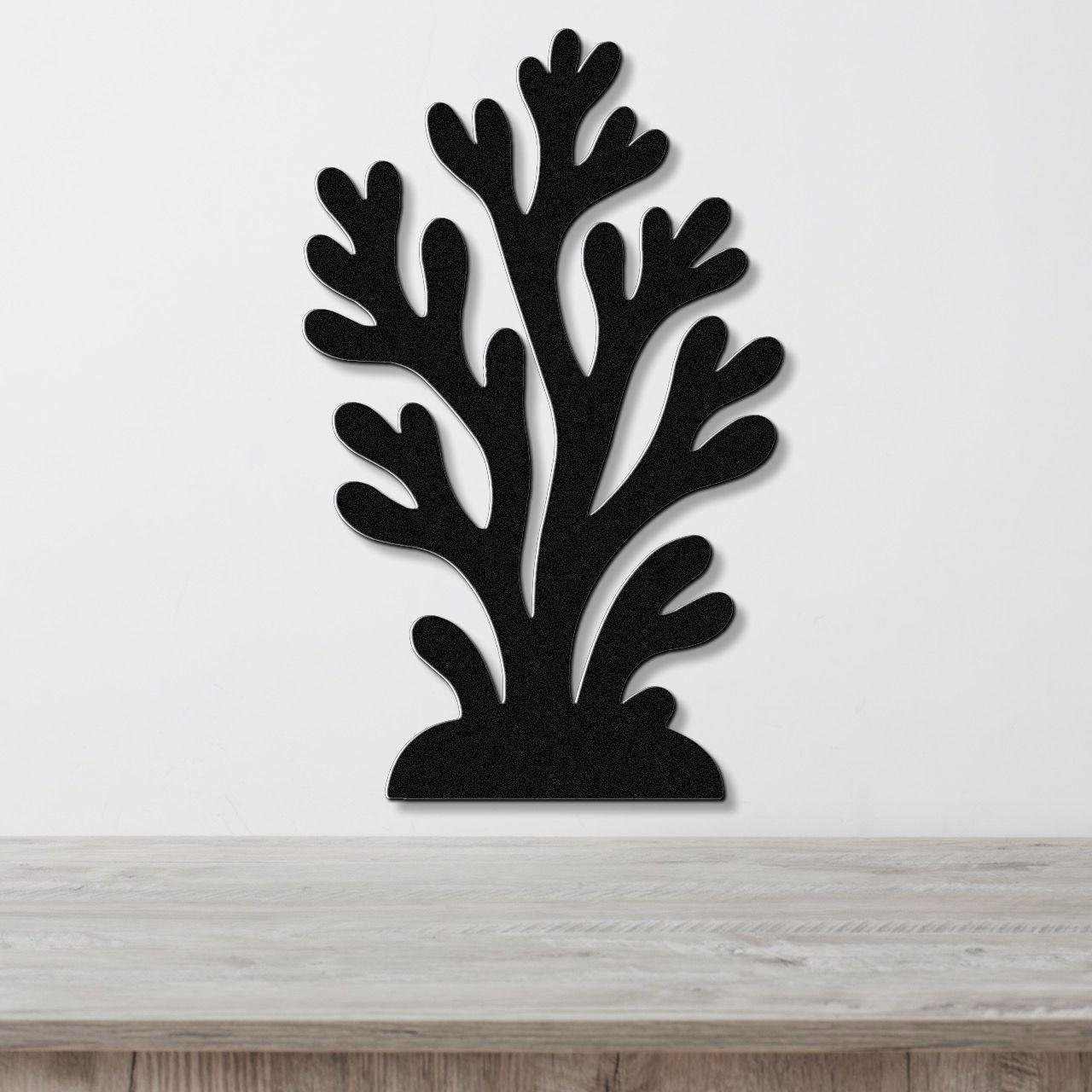 Black metal wall art in a coral silhouette design with branching cutouts, mounted on a white wall above a light wood surface.