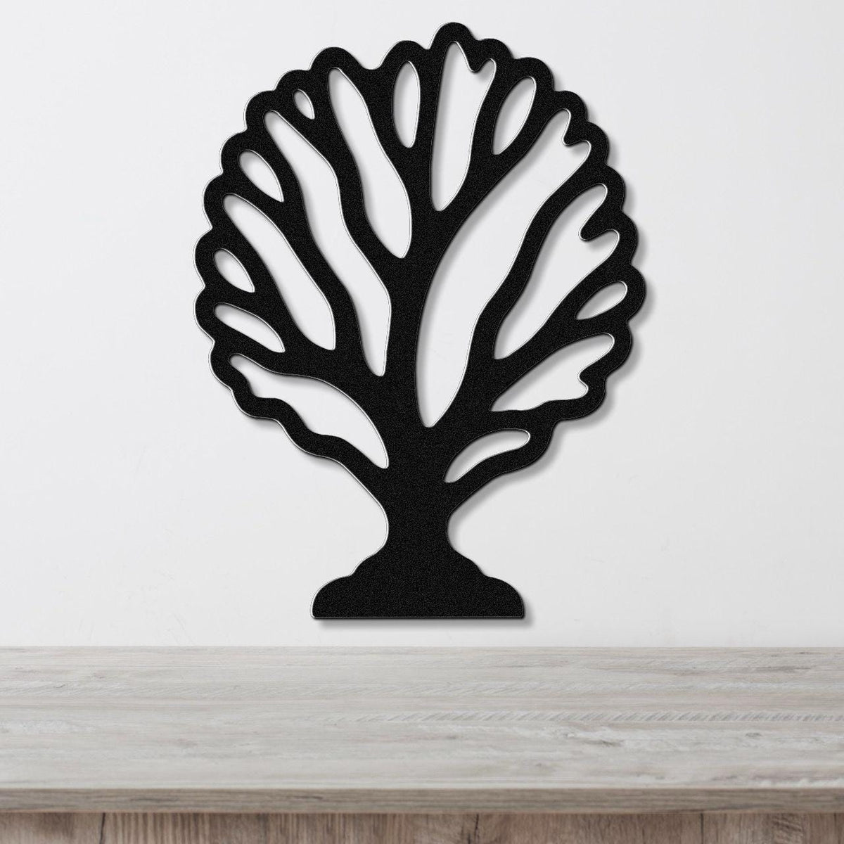 Black metal wall art in a fan coral silhouette with intricate branching cutouts, mounted on a white wall above a light wood surface.