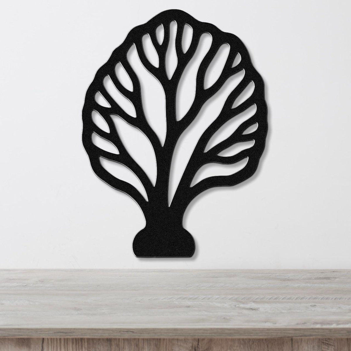 Black metal wall art in a fan coral silhouette with intricate internal cutouts, mounted on a white wall above a light wood surface.