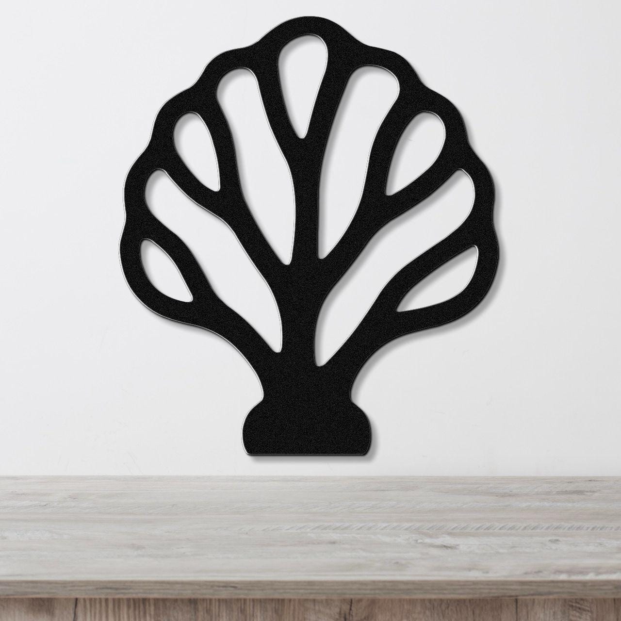 Black metal wall art in a fan coral silhouette with internal cutout branches, mounted on a white wall above a light wood surface.
