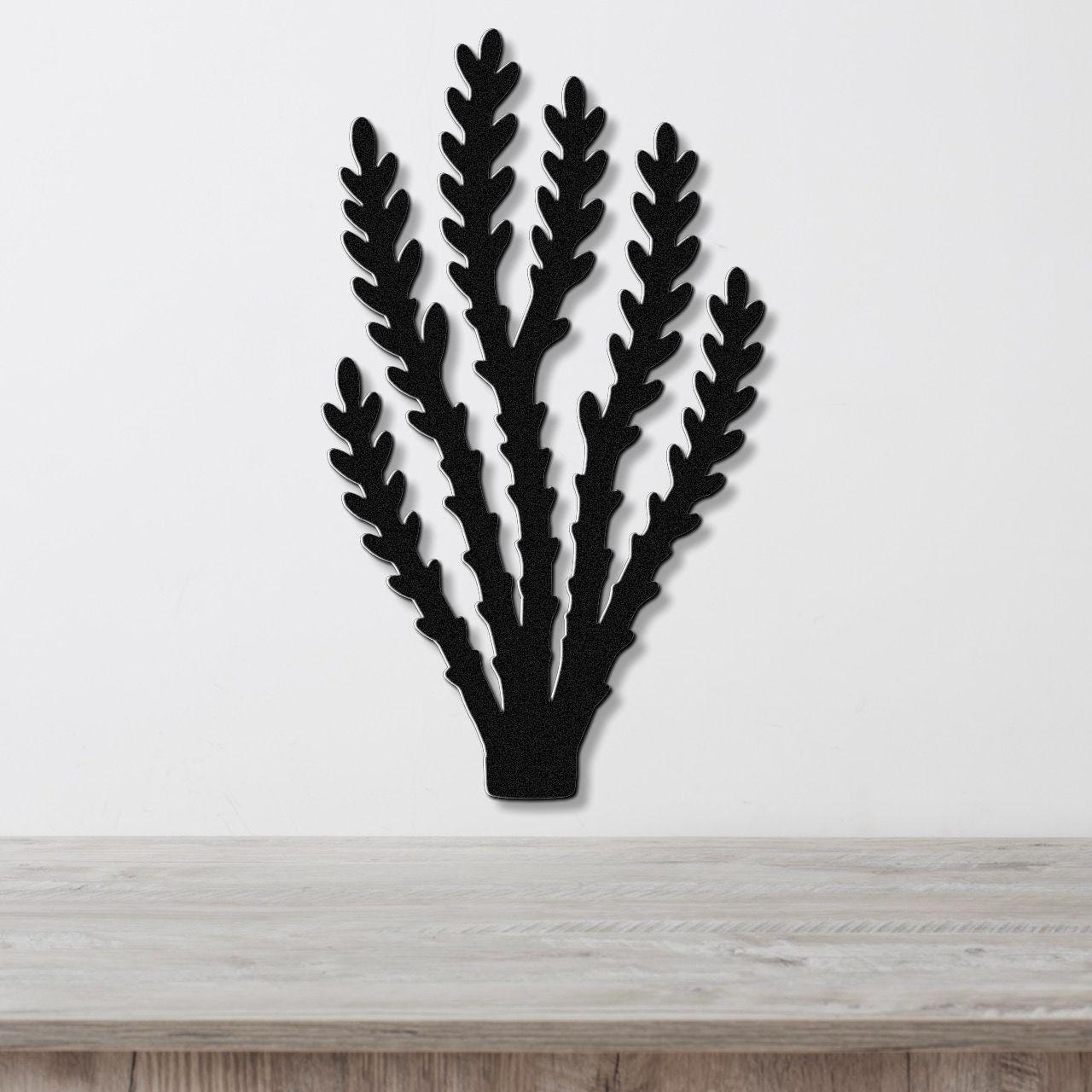 Black metal wall art in a desert branch silhouette with layered cutouts, mounted on a white wall above a light wood counter.