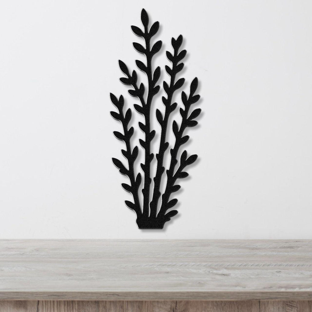 Black metal wall art in a silhouette of desert branches with layered leaf cutouts, mounted on a white wall above a light wood surface.