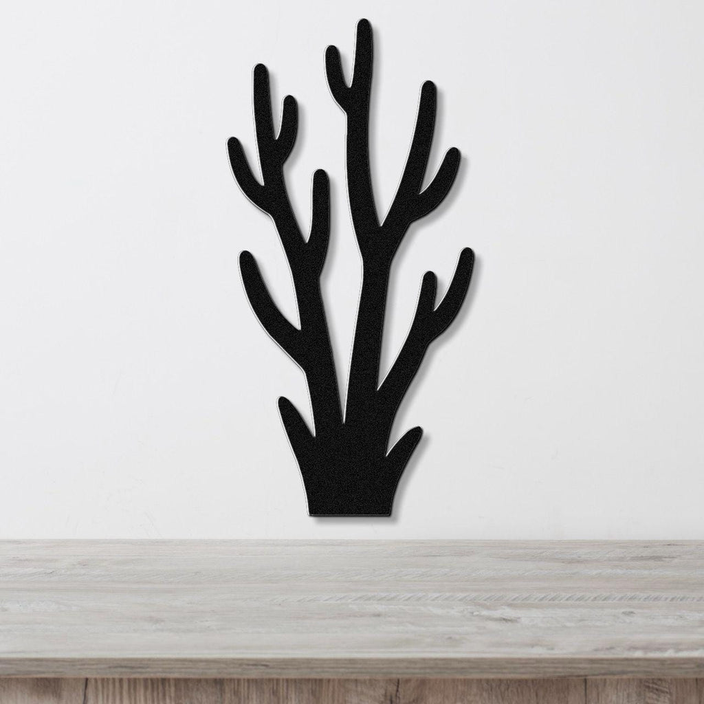 Black metal wall art in a coral or branch silhouette design, mounted on a white wall above a light wood surface.