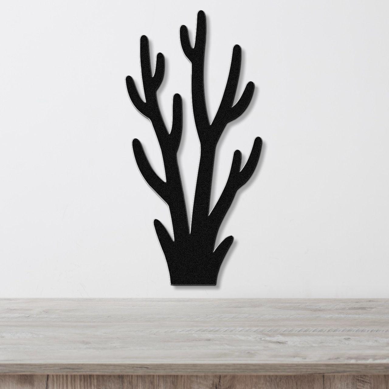 Black metal wall art in a coral or branch silhouette design, mounted on a white wall above a light wood surface.