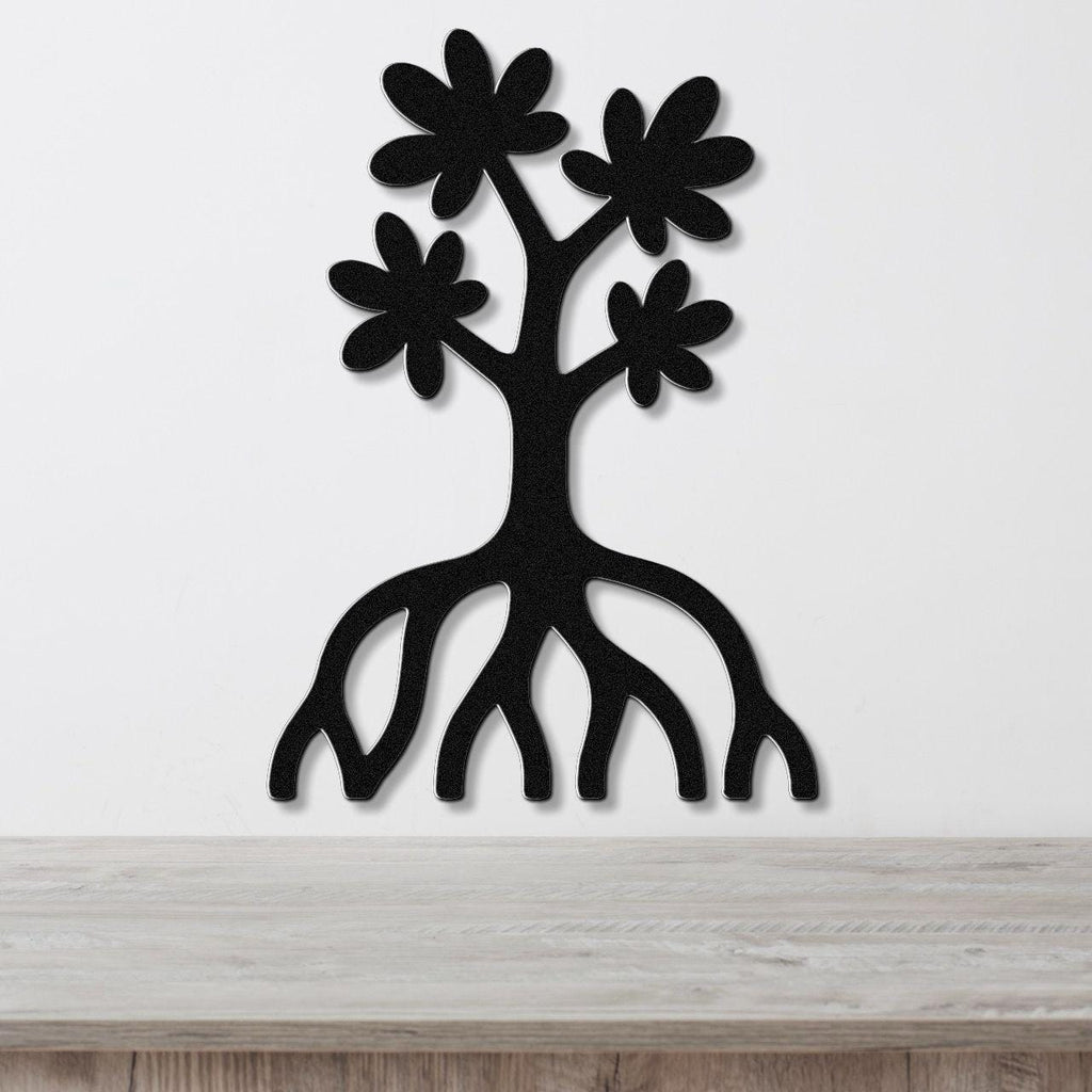 Black metal wall art in the shape of a tree with flower cutouts and exposed roots, mounted on a white wall above a wooden surface.
